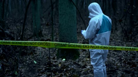 Forensic-analyst-in-white-protective-gear-working-with-evidence-at-crime-scene