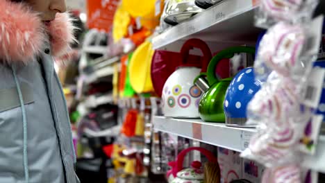 A-young-woman-chooses-a-green-steel-kettle-in-the-supermarket.