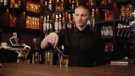 Joven-barman-en-la-barra-interior-vertiendo-whisky-en-cristal-y-trayendo-para-los-visitantes