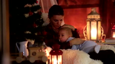 Mother-breastfeeding-her-toddler-son-sitting-in-cozy-armchair-near-Christmas-tree,-wintertime