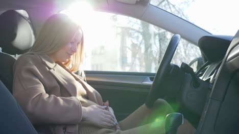 expectant-mom-closes-the-car-door-and-puts-on-the-seat-belt-sitting-in-the-vehicle-in-backlight