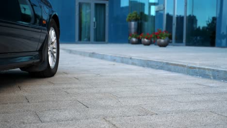 Black-car-stops-near-modern-business-building.-Automobile-drives-up-to-office.-Businessman-commuting-to-work.-Driver-being-on-his-way-to-job.-Cityscape-background.-Slow-motion-Close-up-Low-angle-view