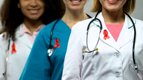 Female-doctors-with-red-ribbons-posing-for-camera,-concept-of-AIDS-awareness