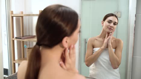 Pflege-der-Haut.-Frau-Gesicht-berühren-und-Blick-auf-den-Spiegel-im-Badezimmer