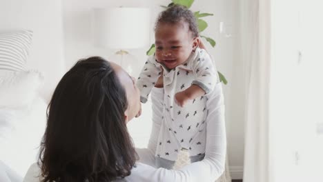 Millennial-mixed-race-mother-lifting-her-baby-and-smiling-at-him,-over-shoulder-view