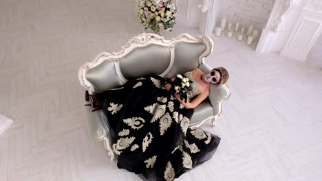 A-creepy-woman-in-a-dress-and-with-makeup-in-form-of-a-skull-lies-on-retro-sofa