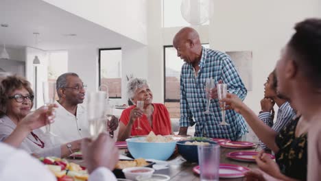 Großvater-steht-am-Esstisch-und-schlägt-einen-Toast-während-einer-Familienfeier-vor