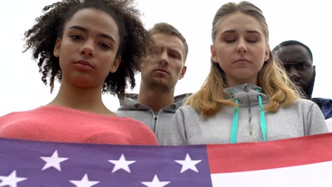 Young-people-silently-holding-American-flag-honoring-shooting-victims,-mourn