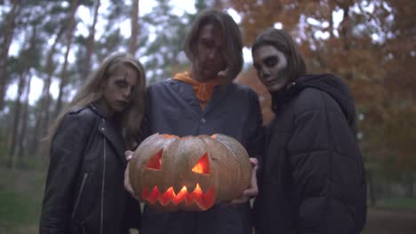 Drei-kaukasische-Freunde-mit-entsetzlichem-Halloween-Make-up-stehen-abends-im-Herbstpark.