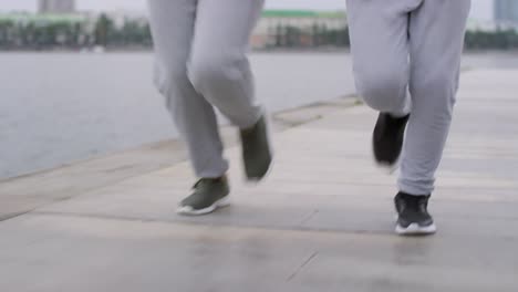 Beine-von-Mutter-und-Sohn-joggen-auf-dem-Riverside-Sidewalk