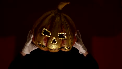 Scary-man-in-the-makeup-of-a-clown-holds-a-pumpkin-for-Halloween-and-puts-it-on-his-head.Terrible-clown-puts-on-a-mask-in-the-shape-of-a-pumpkin-on-his-head.-Terrible-clown-holds-in-his-hands-a-Jack-O-Lantern-with-luminous-eyes-and-a-mouth.