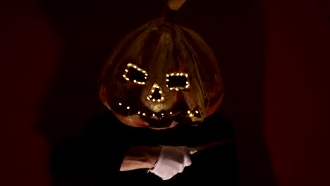 Scary-man-with-a-pumpkin-head-and-luminous-eyes-looks-at-the-camera.-Man-with-a-pumpkin-head-scares-raising-his-hands-up.-Halloween.