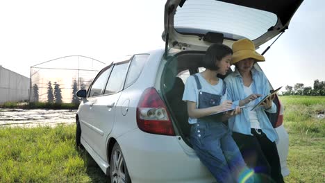 Familia-asiática-inteligente-sentada-en-el-coche-y-el-uso-de-la-tableta-digital-para-el-acceso-a-Internet-frente-a-la-casa-verde,-concepto-de-agricultura-inteligente