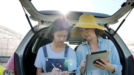 Smart-Asian-family-sitting-on-car-and-using-digital-tablet-for-internet-access-front-of-green-house,-Smart-agriculture-concept