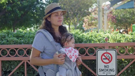 Frau-und-Baby-in-Trage-stehen-neben-No-Smoking-Zeichen-im-Park