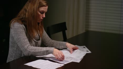 A-woman-looking-over-bills-at-the-table,-looking-stressed