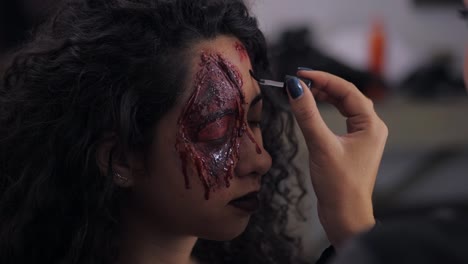 Make-up-artist-make-the-girl-halloween-make-upin-studio.Halloween-face-art.Woman-applies-on-professional-greasepaint-on-the-face-of-spanish-girl.War-paint-with-blood,-scars-and-wounds.Slow-motion