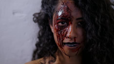 Aterrador-retrato-de-niña-con-maquillaje-de-Halloween-sangre.-Hermosa-mujer-latina-con-cabello-rizado-en-cámara-en-estudio.-Maquillaje-muerto-viviente.-Cámara-lenta