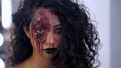 Aterrador-retrato-de-niña-con-maquillaje-de-Halloween-sangre.-Hermosa-mujer-latina-con-cabello-rizado-en-cámara.-Cámara-lenta