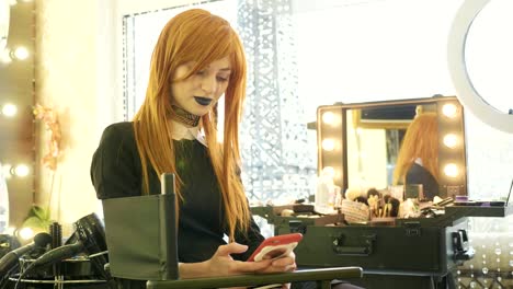 Junge-schöne-Mädchen-mit-Halloween-Make-up-mit-Smartphone-im-Schönheitssalon