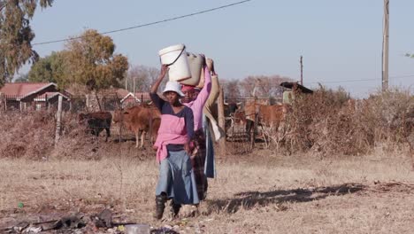 Tres-mujer-africana-llevando-agua-en-la-cabeza-en-cubos-de-plástico-de-un-origen-remoto-y-caminando-hacia-sus-casas