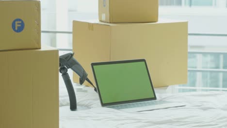 Dolly-shot:-laptop-computer-with-green-screen-chroma-key-on-the-bed-with-cardboard-boxes-around,-Online-business-concept.