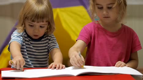 Two-little-children-girl-and-boy-sitting-at-table-drawing.-Brother-and-sister-drawing-with-colorful-crayons