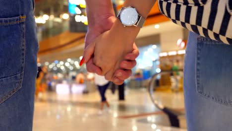 Young-couple-holding-hands-of-each-other-and-walking-at-terminal-of-airport.-Man-and-woman-taking-arms-and-stepping-during-trip.-Symbol-of-love-and-devotion.-Close-up-Rear-back-view