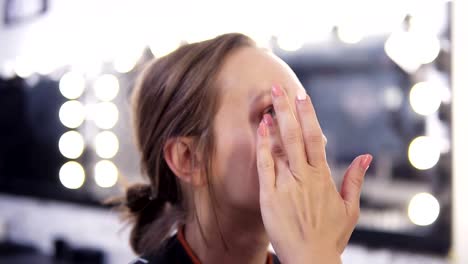 Makeup-artist-applies-foundation-of-a-beautiful-young-girl-in-the-makeup-studio-using-fingers-and-brush.-Close-up