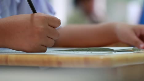 Bildung-Testkonzept:-Hände-Schüler-halten-Stift-für-Prüfung-Prüfungen-schreiben-Antwortbogen-oder-Übung-für-die-Aufnahme-in-Prüfung-Kohlepapier-Computer-auf-Holztisch-im-Klassenzimmer-in-der-High-School-zu-füllen