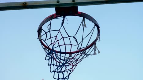 Lanzar-bola-en-el-aro-de-baloncesto-contra-el-cielo-azul,-a-través-de-aro,-al-aire-libre