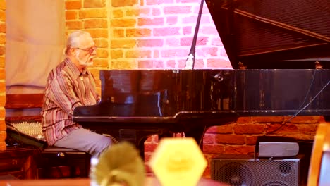 Hombre-de-pelo-gris-con-una-cola-en-la-cabeza-con-gafas-tocando-el-piano-en-un-bar-de-jazz