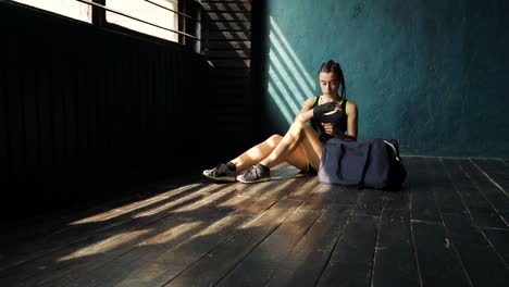 Panning-young-beautiful-woman-sitting-on-floor-and-wrapping-hands-with-black-boxing-wraps-in-club.