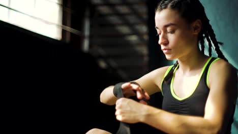 Closeup-young-beautiful-woman-sitting-on-floor-and-wrapping-hands-with-black-boxing-wraps-in-club.