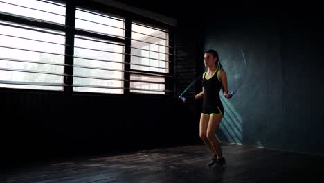 Young-purposeful-serious-female-boxer-in-wrapped-bandage-fist-hands-jumping-on-skipping-rope-in-gym