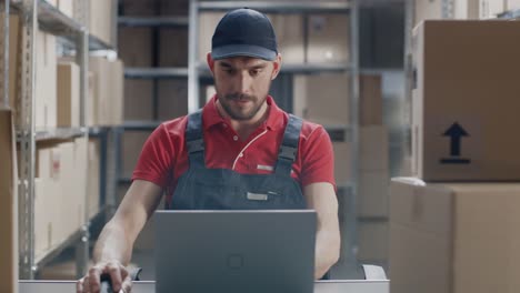 Uniformed-Worker-Uses-Laptop-while-Sitting-at-His-Desk-in-the-Warehouse.