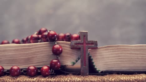 Bibel-und-Kreuz-Perlen-auf-einem-goldenen-Tisch-öffnen,-Nahaufnahme.-Schönen-dunklen-Hintergrund.-Religion-Konzept