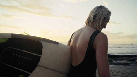 A-blonde-wet-surfer-girl-smiling-while-walking-with-a-surfboard-in-her-hands.