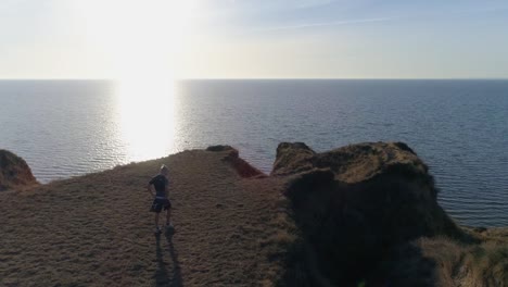 sports-training-on-open-air,-man-in-sportswear-walks-on-slope-to-water-on-nature-against-sky-in-bright-sunlight