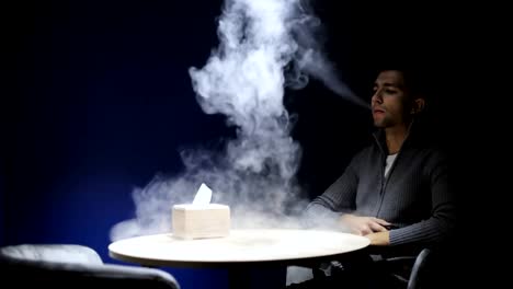 Young-man-sitting-on-the-bar-smoking-e-cigarette-vape-in-the-dark-cafe