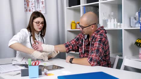 The-doctor-unwinds-the-elastic-bandage-the-damaged-wrist-of-a-male-patient.