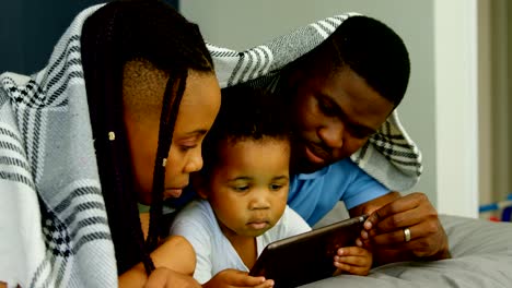 Side-view-of-young-black-family-using-digital-tablet-on-bed-in-bedroom-of-comfortable-home-4k