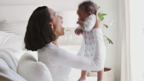 Millennial-mixed-race-mother-lifting-her-baby-and-kissing-his-tummy