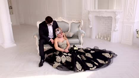 Couple-with-a-creepy-Halloween-makeup-sit-on-a-vintage-sofa-in-a-vintage-room.