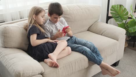 Girl-with-her-brother-playing-game-using-mobile-phone-on-sofa