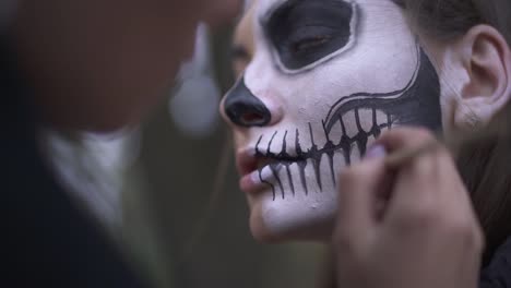 Woman's-hands-applying-black-paint-on-the-face-of-the-girl-using-the-small-brush-close-up.