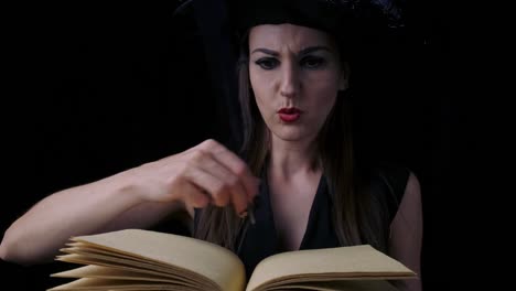 Attractive-mystical-witch-woman-with-bright-red-lips-on-a-black-background,-writes-in-a-book-with-a-bird-feather,-casting-spells.-Halloween-concept