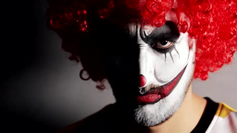 Cara-enojada-malvada-con-makup-de-payaso-de-miedo-mira-a-la-cámara-en-la-oscuridad-en-Halloween