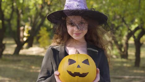 En-serio,-la-chica-pelirroja-caucásica-vestida-con-traje-de-bruja-de-Halloween-de-pie-en-el-parque-de-otoño.