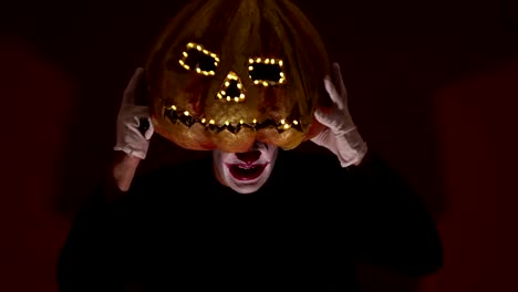 Gruseliger-Mann-mit-Kürbiskopf-und-leuchtenden-Augen-schaut-in-die-Kamera.-Mann-mit-Kürbiskopf-erschreckt,-die-Hände-hochzuheben.-Halloween.